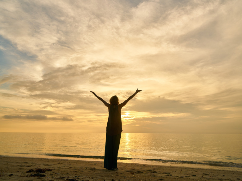 Woman with arms raised up standing on the beach allowing herself to be open and blessed
