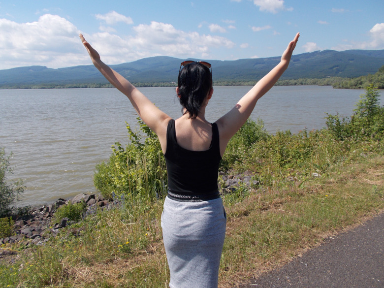 Woman standing near waters edge with arms outstretched dreaming of manifesting desires