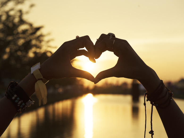 Woman hands made made into a heart, bright sunlight and water. loved and supported symbol