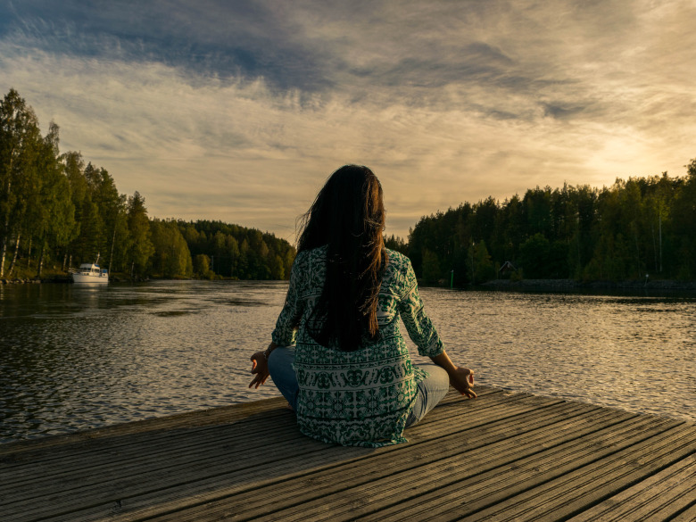 Woman sitting on a dock meditating reconnecting to her true self