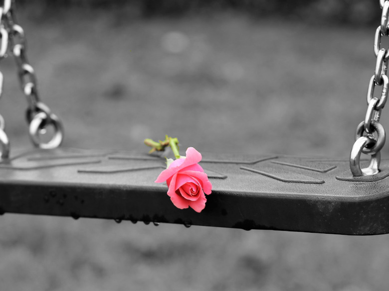 A Childs swing on a swing set stopped with a rose draped on it.