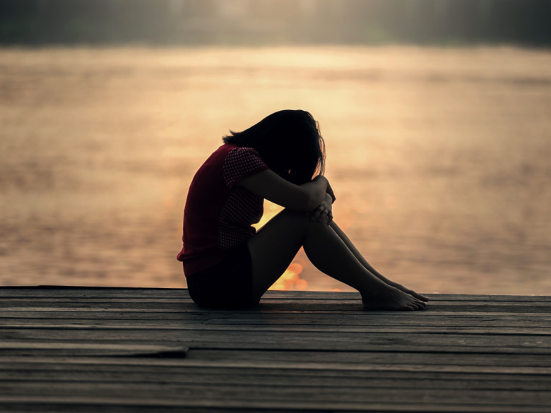 Girl sitting with her head on her knees with early morning sadness